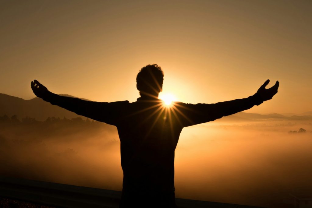 A man looking at sunrise with open arms